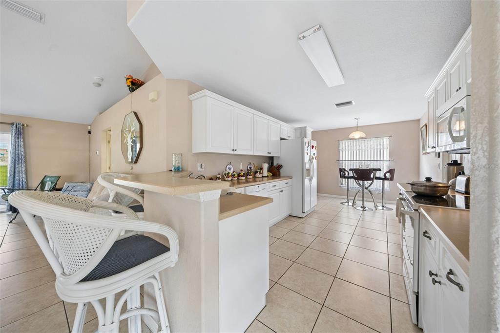 A kitchen with white cabinets, tan countertops, and tile flooring opens to a dining area — 140 MORNING GLORY CIRCLE, WINTER HAVEN, FL