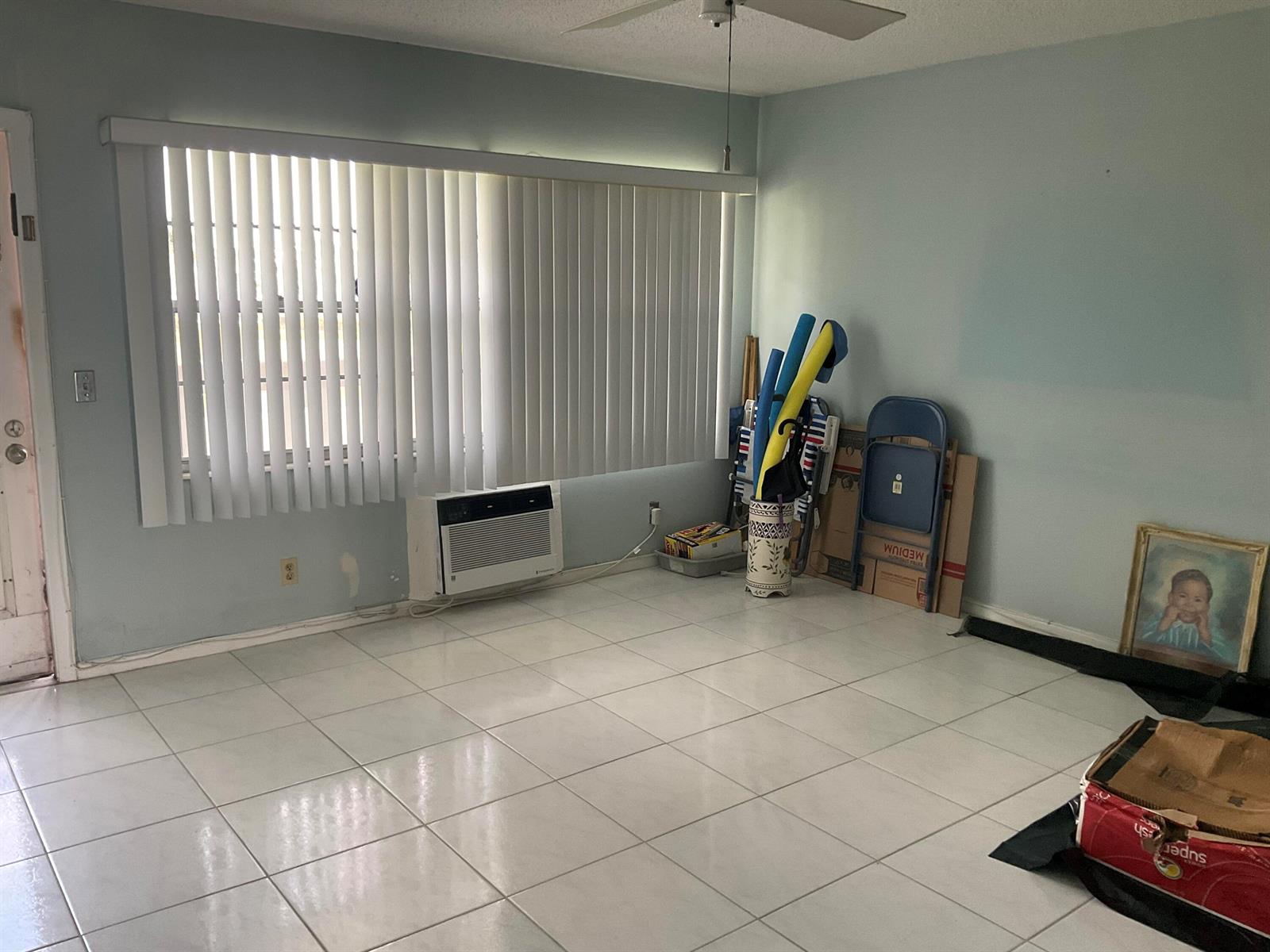 A room with light blue walls, white tile flooring, vertical blinds, and a window air conditioner — 189 E Preston Way, Boca Raton FL 33434, BOCA RATON, FL