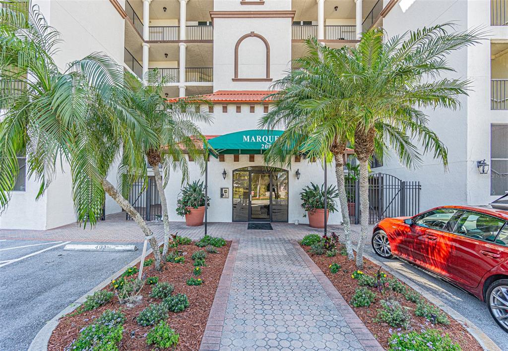 The exterior entrance of a multi-story building features a green awning and palm trees — 200 121ST AVENUE UNIT 304, TREASURE ISLAND, FL