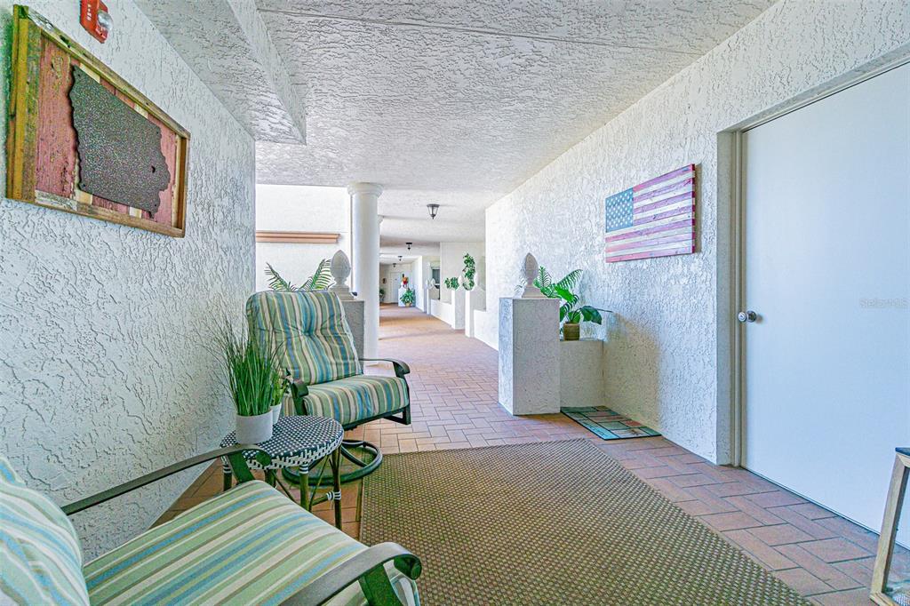 An outdoor covered walkway features a seating area with two chairs and a small table — 200 121ST AVENUE UNIT 304, TREASURE ISLAND, FL