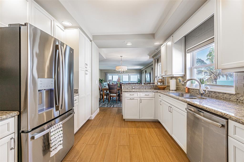 A kitchen with white cabinets, stainless steel appliances, and wood-look flooring opens to a dining area — 200 121ST AVENUE UNIT 304, TREASURE ISLAND, FL
