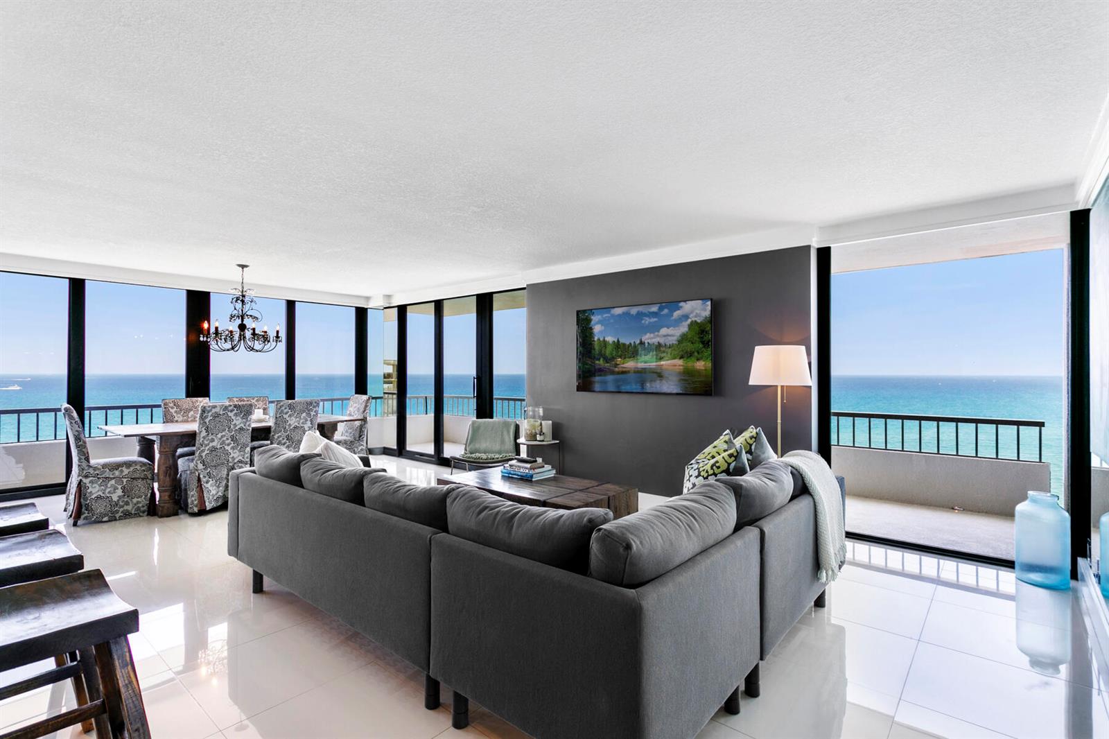 A living and dining area with a gray sectional, dark accent wall, and ocean views — 5510 N Ocean Drive # 12a, Singer Island FL 33404, SINGER ISLAND, FL