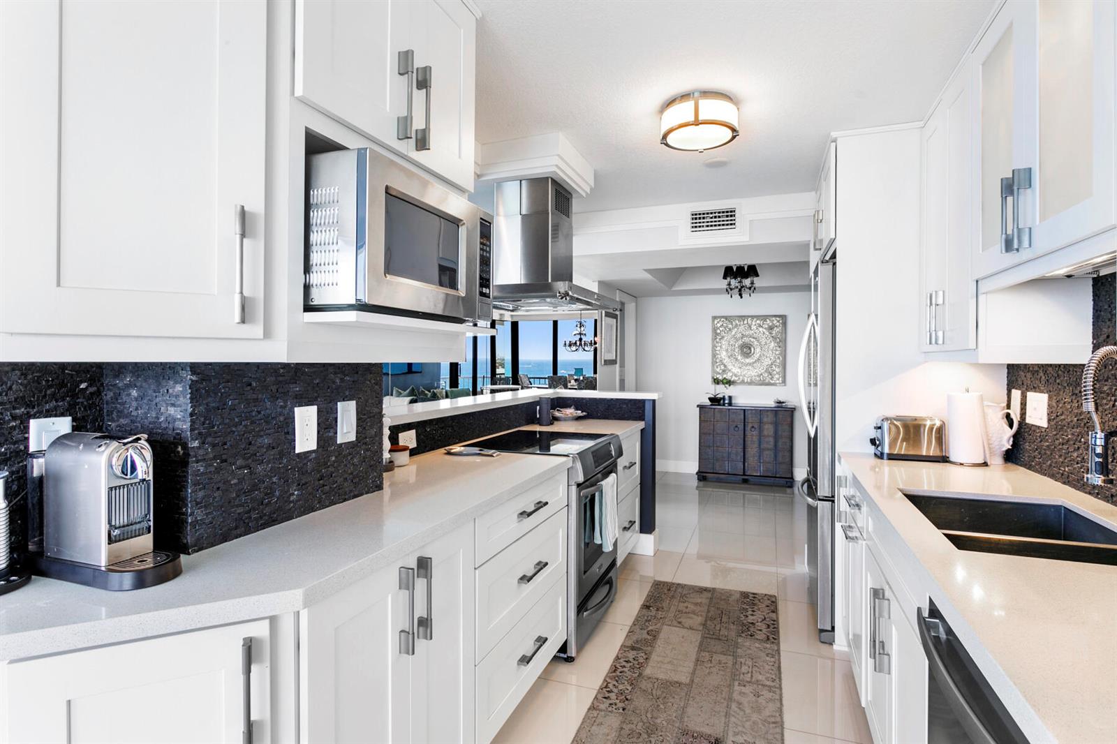 A modern white kitchen features stainless steel appliances, dark stone backsplashes, and quartz countertops — 5510 N Ocean Drive # 12a, Singer Island FL 33404, SINGER ISLAND, FL
