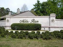 A light-colored masonry wall with the text Mile Run stands behind a row of shrubs — 3760 NW 53RD ROAD, GAINESVILLE, FL
