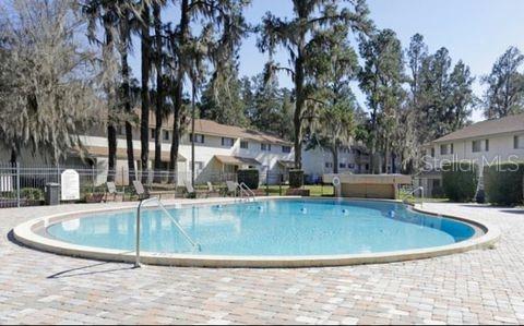A curved outdoor swimming pool sits on a paved patio surrounded by trees and buildings — 3760 NW 53RD ROAD, GAINESVILLE, FL