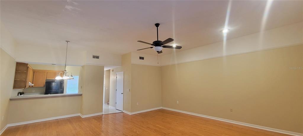 A living room with light-colored walls, wood flooring, and a ceiling fan opens to a kitchen — 3760 NW 53RD ROAD, GAINESVILLE, FL