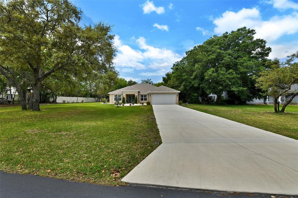 A single-story house with a concrete driveway sits on a large, tree-filled grassy lot — 4255 RACHEL BOULEVARD, SPRING HILL, FL
