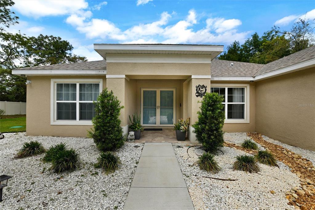 A beige stucco house features a double front door, a concrete walkway, and rock landscaping — 4255 RACHEL BOULEVARD, SPRING HILL, FL