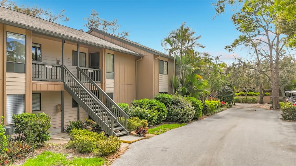 A two-story apartment building with tan siding, a wooden staircase, and surrounding landscaping — 1707 PELICAN COVE ROAD UNIT GL351, SARASOTA, FL