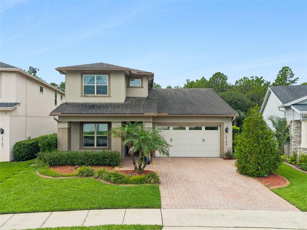 A two-story suburban house features a brick driveway, a two-car garage, and a palm tree — 14156 ALAFAYA OAK BEND, ORLANDO, FL
