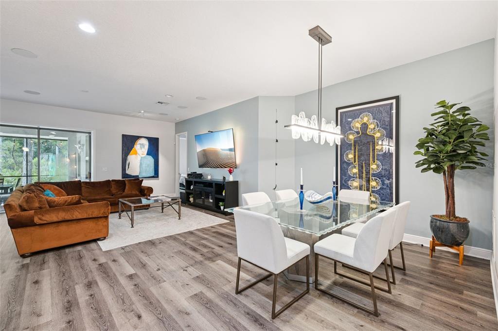 An open-concept living and dining area features wood-look flooring, a brown sectional, and modern decor — 14156 ALAFAYA OAK BEND, ORLANDO, FL