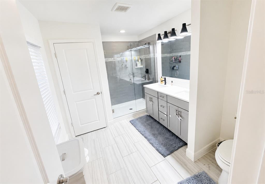A modern bathroom features a gray vanity, a glass-enclosed shower, and light-colored tile flooring — 1378 PARK LEAH CIRCLE, APOPKA, FL