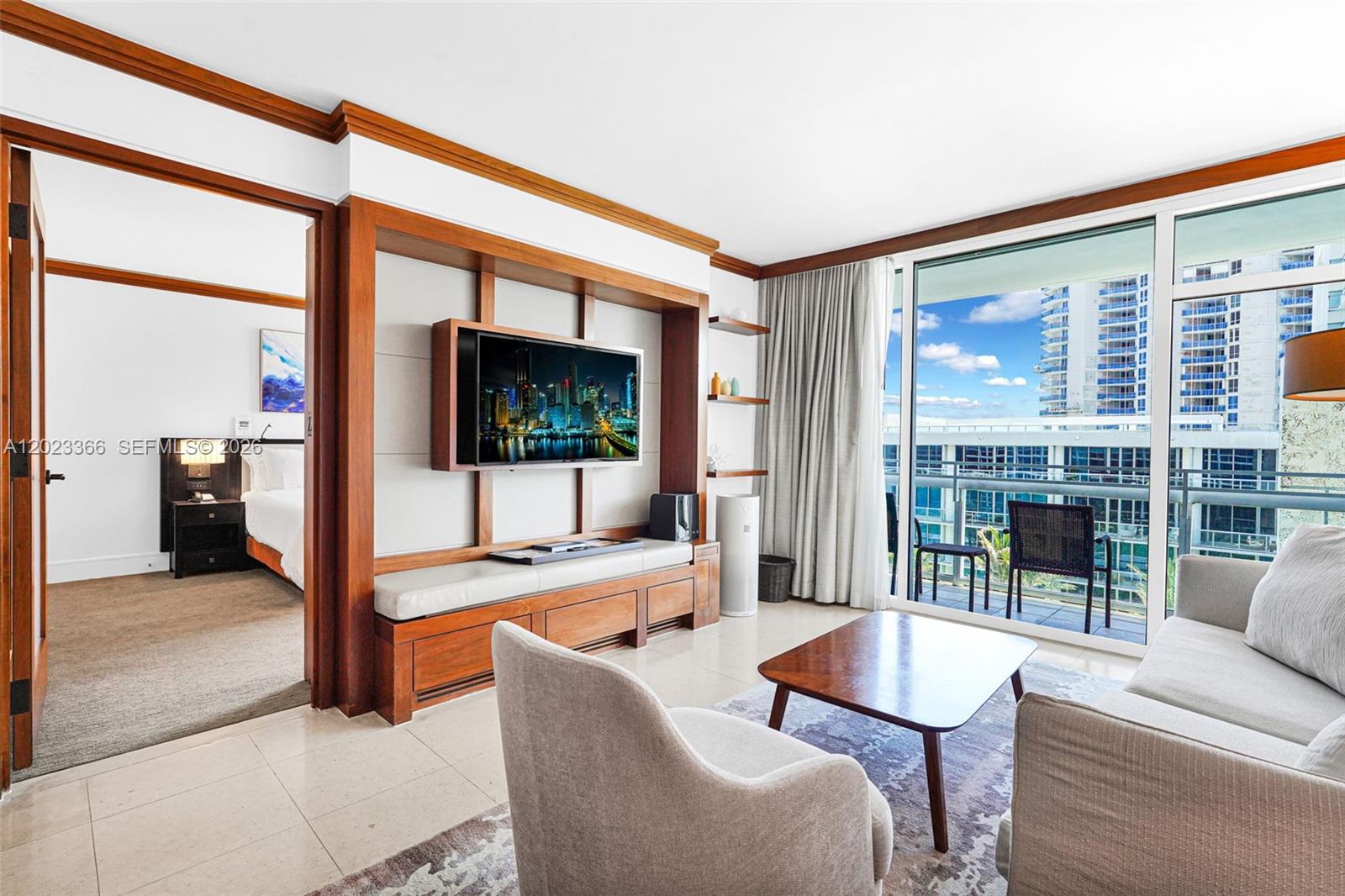 A living room features a built-in wooden media console, a television, and a balcony view — 6801 Collins Ave, Miami Beach FL 33141, MIAMI BEACH, FL