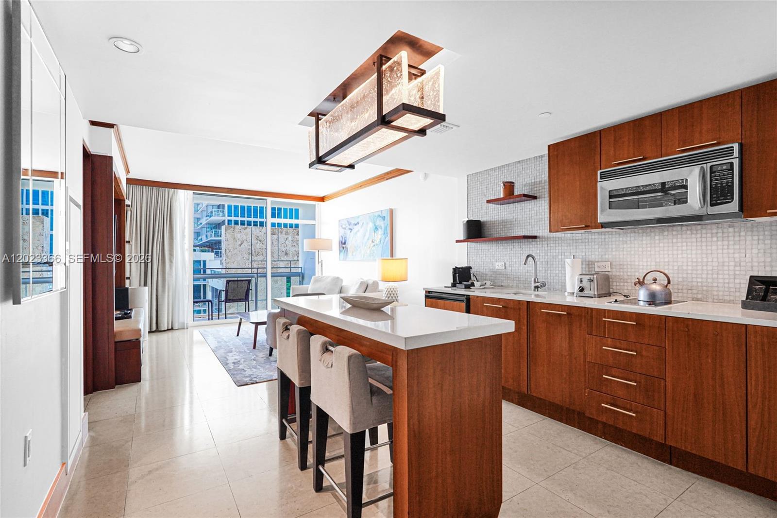 A modern kitchen features wood cabinets, a white island with bar seating, and a balcony — 6801 Collins Ave, Miami Beach FL 33141, MIAMI BEACH, FL