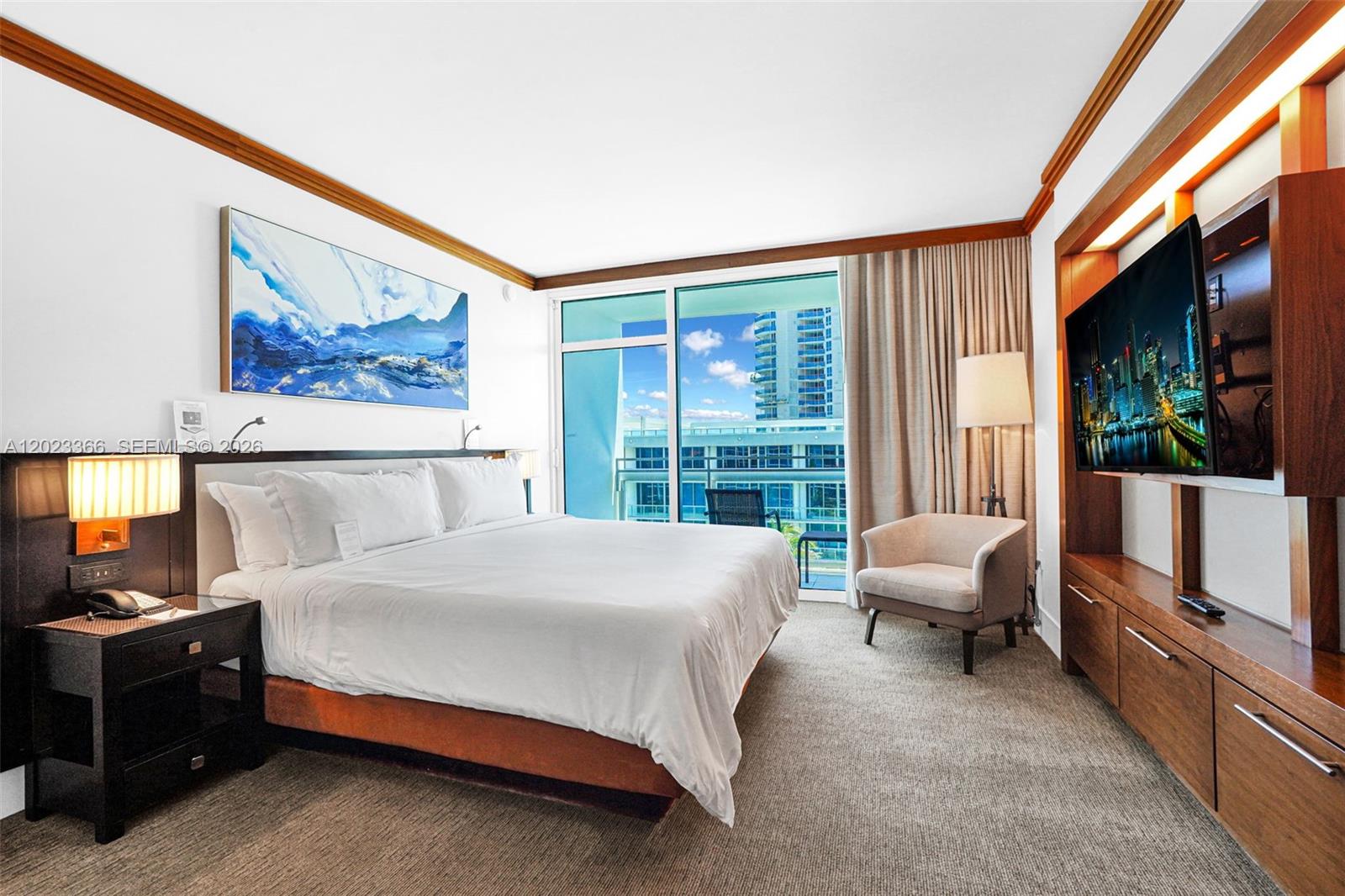 A hotel bedroom features a king bed, a wall-mounted television, and a balcony with views — 6801 Collins Ave, Miami Beach FL 33141, MIAMI BEACH, FL
