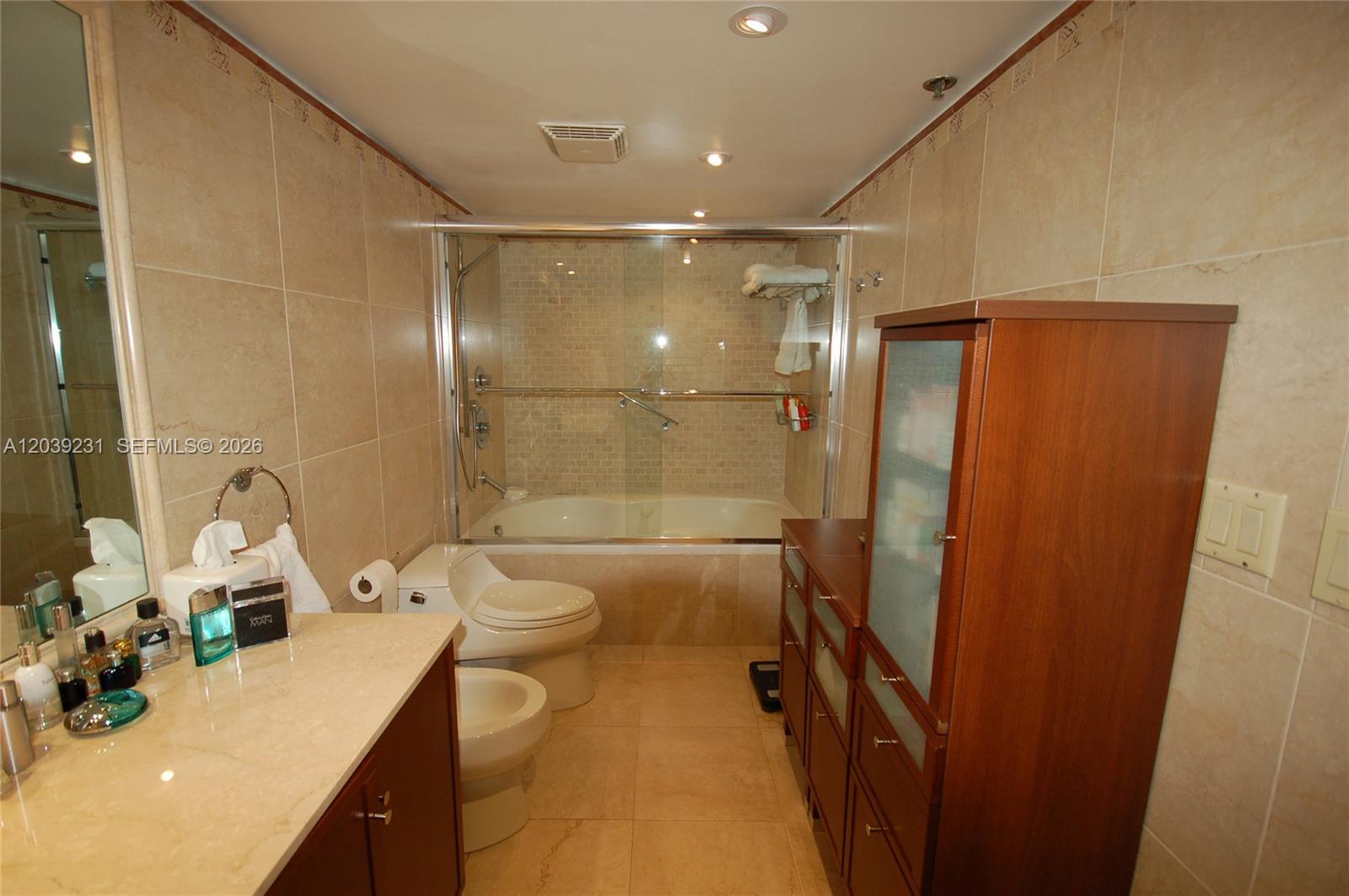 A bathroom features a glass-enclosed tub, a toilet, a vanity, and wood cabinetry — 8877 Collins Ave # 507, Surfside FL 33154, SURFSIDE, FL