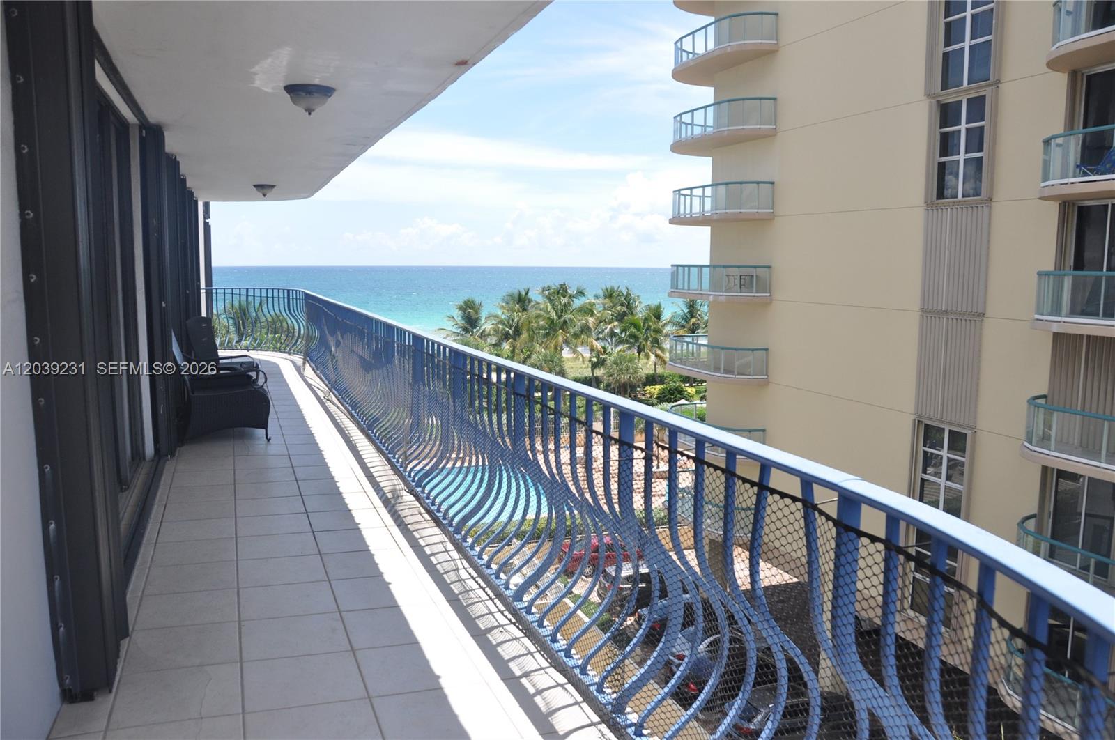 A balcony with a blue metal railing overlooks a swimming pool and the ocean — 8877 Collins Ave # 507, Surfside FL 33154, SURFSIDE, FL
