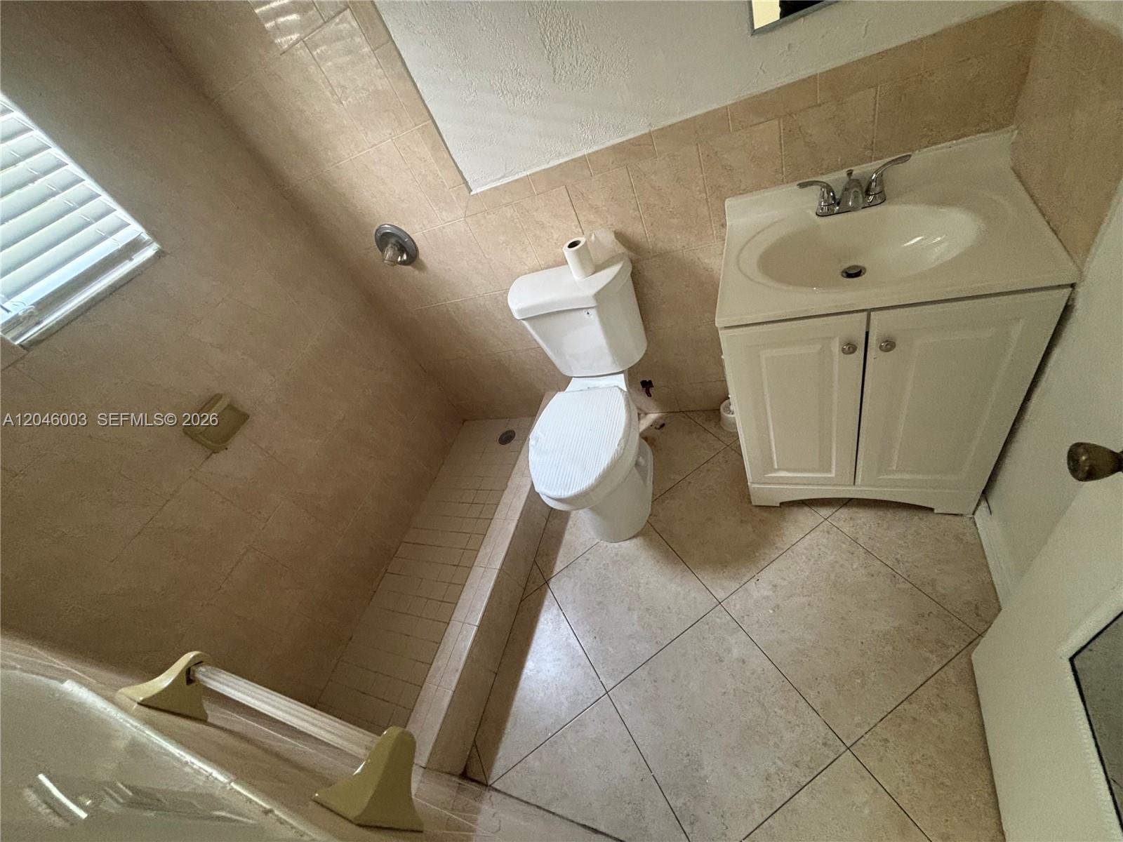 A bathroom features a tiled shower, a white toilet, and a vanity with a sink — PEMBROKE PINES, FL