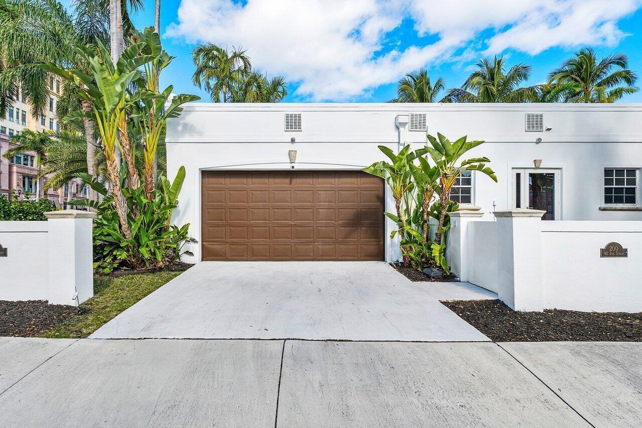 A white exterior building features a brown garage door, a driveway, and tropical landscaping — 200 NE 2nd Street, Boca Raton FL 33432, BOCA RATON, FL