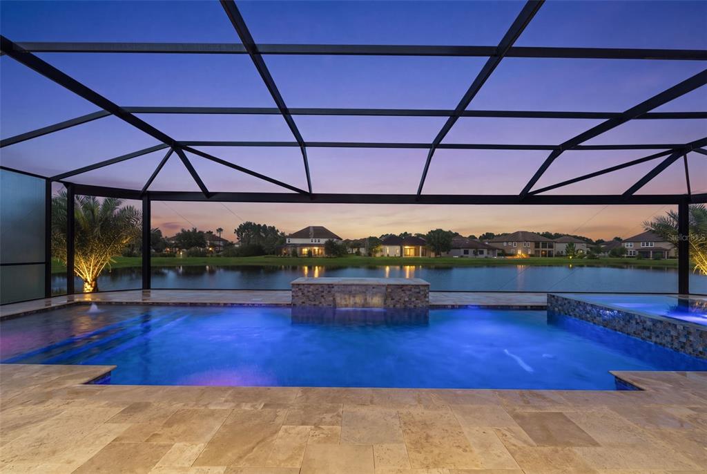A screened-in pool patio overlooks a lake at sunset with a stone water feature — 33161 KATELAND DRIVE, WESLEY CHAPEL, FL
