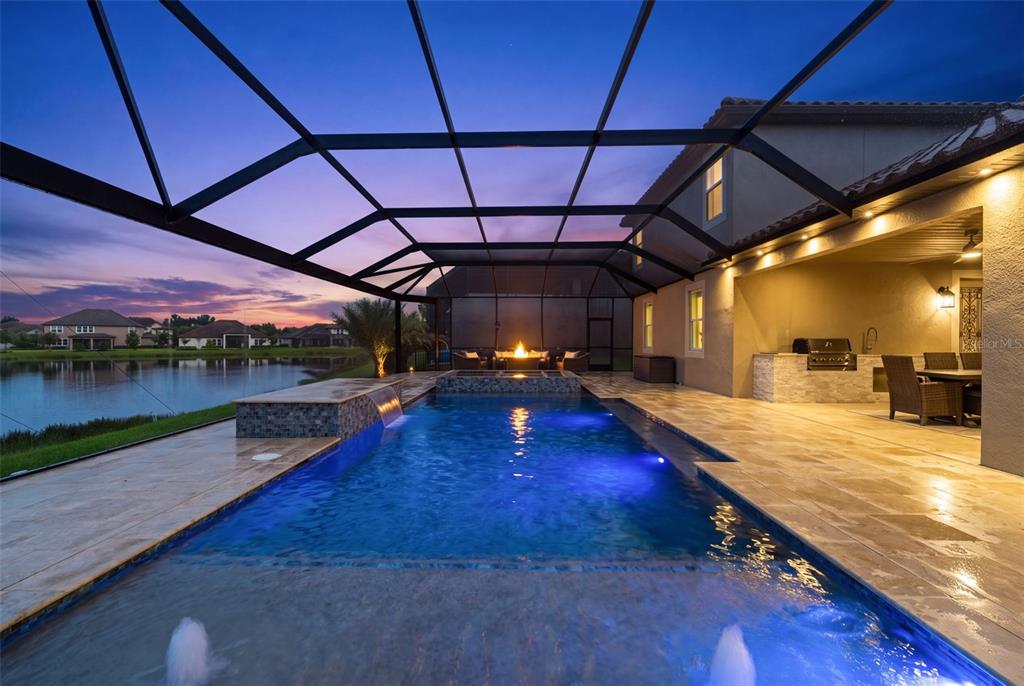 A screened-in patio features a swimming pool with fountains, a fire pit, and outdoor kitchen — 33161 KATELAND DRIVE, WESLEY CHAPEL, FL
