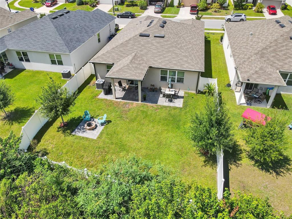 An aerial view shows a backyard with a patio, fire pit, and white vinyl fencing — 4548 ORCHARD GROVE ROAD, ST CLOUD, FL