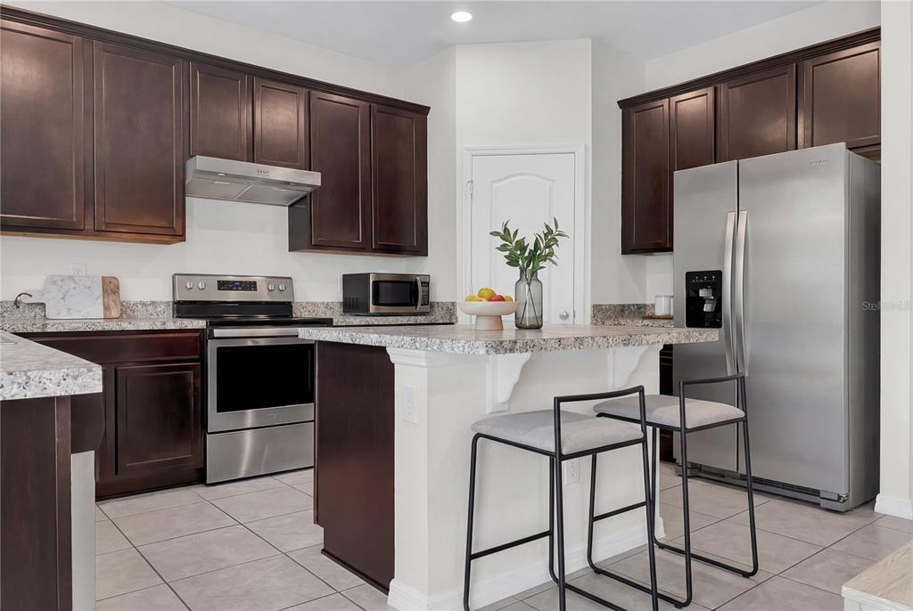 A kitchen with dark wood cabinets, stainless steel appliances, granite countertops, and a breakfast bar — 4548 ORCHARD GROVE ROAD, ST CLOUD, FL