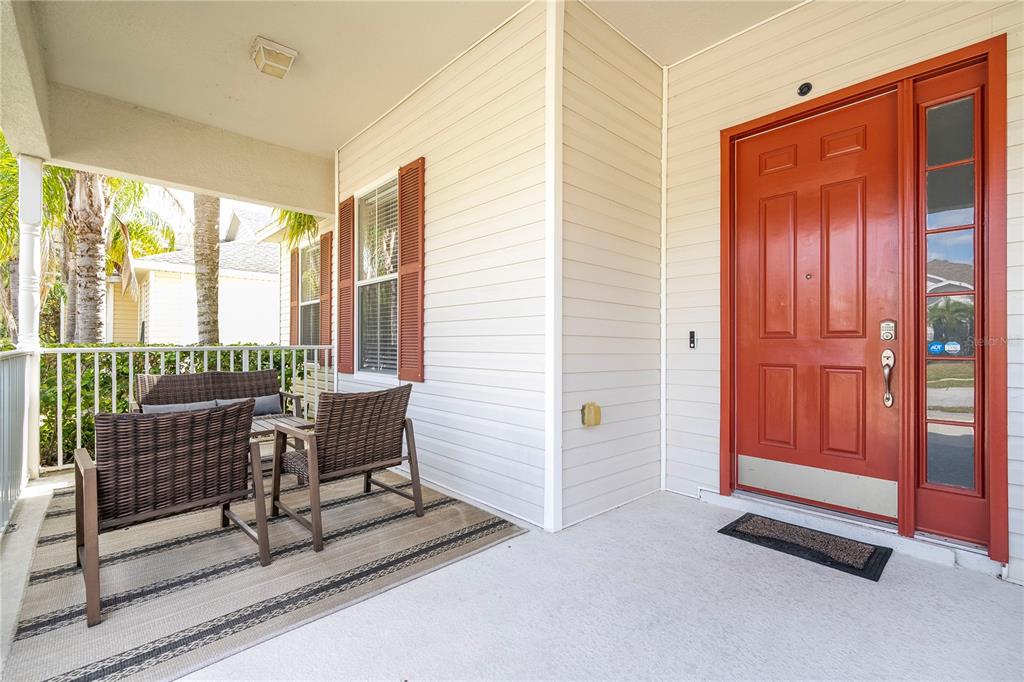 A covered front porch features a red door, light siding, and outdoor patio furniture — 4978 STRAND STREET UNIT 0, KISSIMMEE, FL
