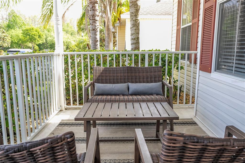 A covered porch features a wicker loveseat, a coffee table, and two chairs — 4978 STRAND STREET UNIT 0, KISSIMMEE, FL
