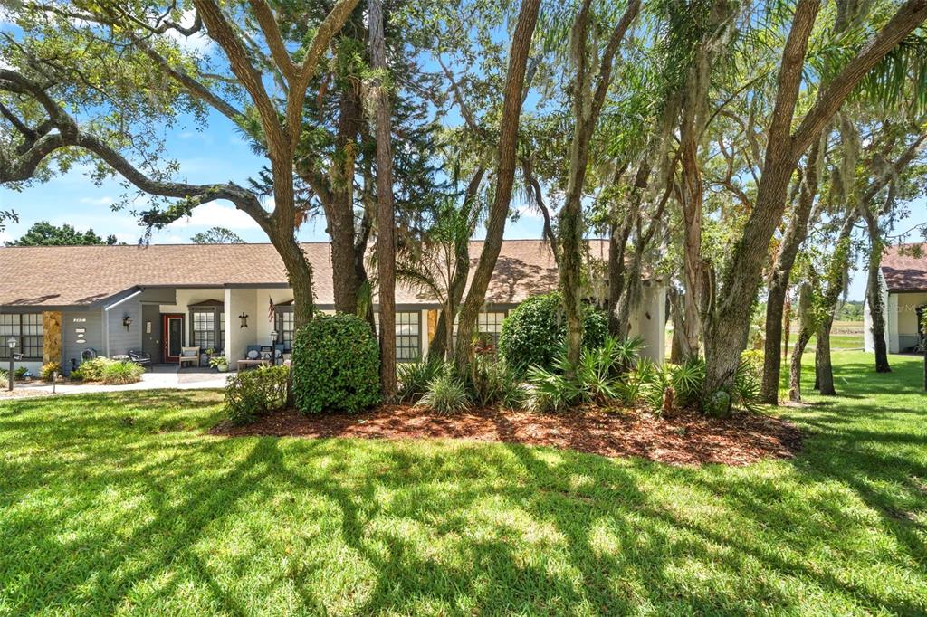 A single-story residential building with a brown shingled roof is partially obscured by large trees — 6410 NATURE PRESERVE LANE, SPRING HILL, FL