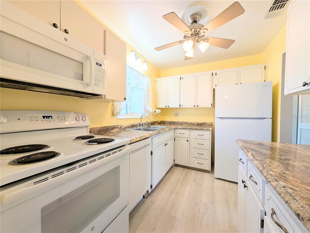 A kitchen with white cabinets, light-colored flooring, yellow walls, and white appliances — 1830 SUNNY DRIVE UNIT D31, BRADENTON, FL