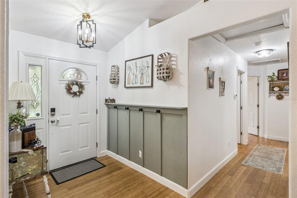 A bright entryway features wood floors, a white front door, and a green paneled wall — 214 MOUNTAIN DRIVE, BABSON PARK, FL