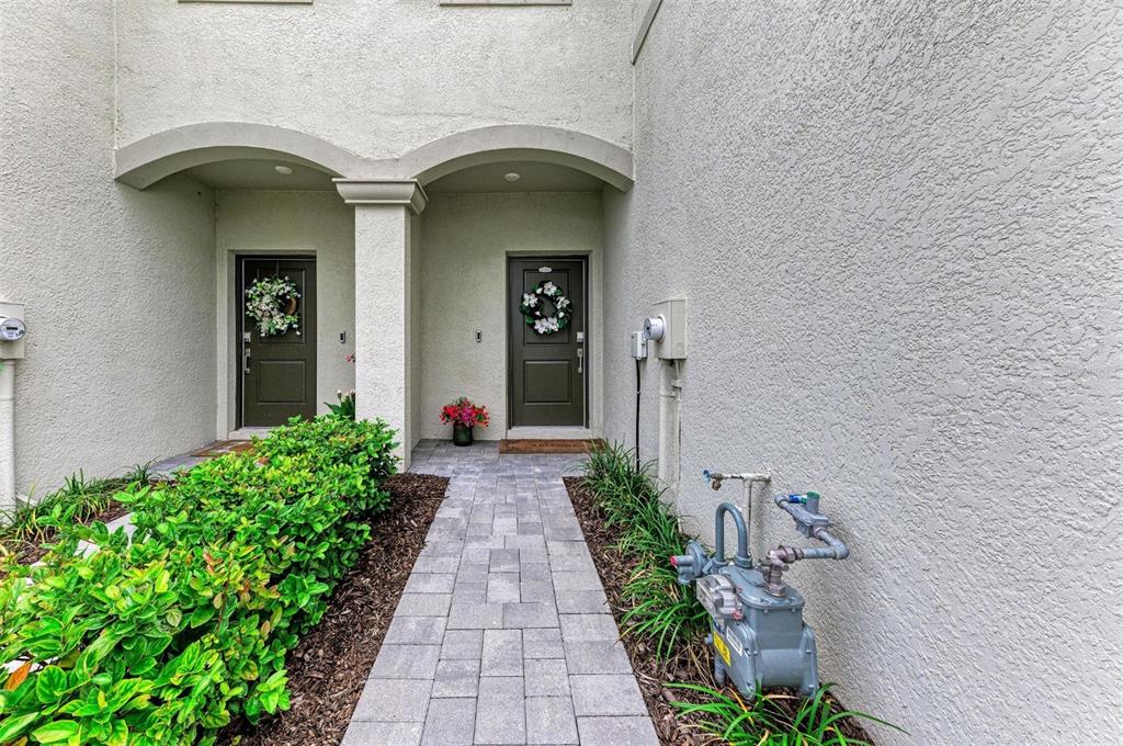 A paved walkway leads to two dark front doors under arched entryways with stucco walls — 14767 LYLA TERRACE, LAKEWOOD RANCH, FL