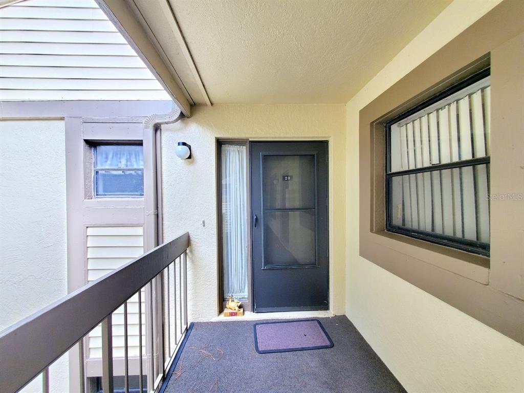 An exterior view of a residential apartment entrance with a dark door and balcony railing — 20 WOODLAKE PLACE UNIT 20, OLDSMAR, FL