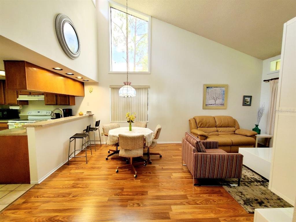 An open-concept living and dining area features wood-look flooring, vaulted ceilings, and a kitchen bar — 20 WOODLAKE PLACE UNIT 20, OLDSMAR, FL