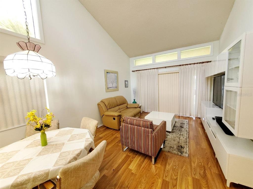 A living and dining area features vaulted ceilings, wood-look flooring, and a white entertainment unit — 20 WOODLAKE PLACE UNIT 20, OLDSMAR, FL