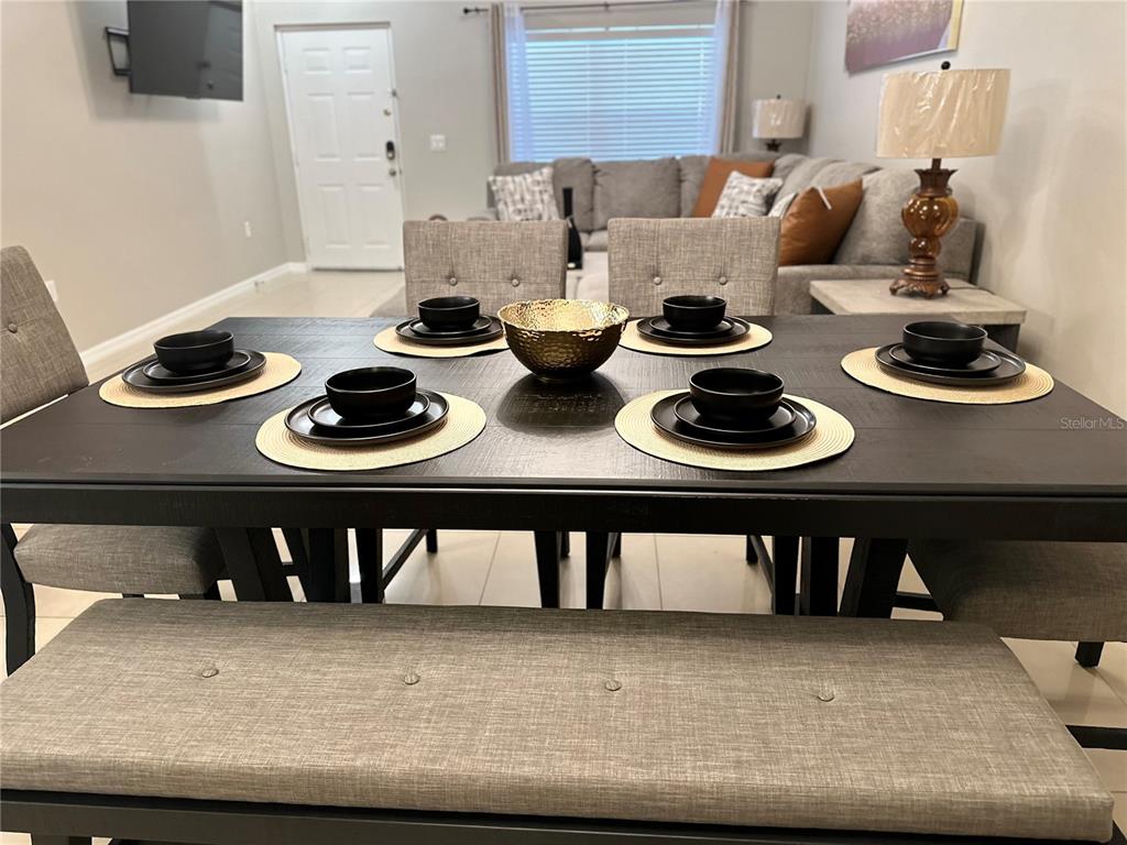 A dining table with place settings and a bench sits in front of a living room — 3107 SUN LAKE COURT UNIT B, KISSIMMEE, FL
