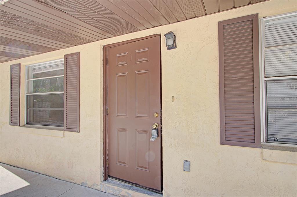 A brown front door with a lockbox sits between two windows with brown shutters — 830 N CLAKE STREET, DELAND, FL