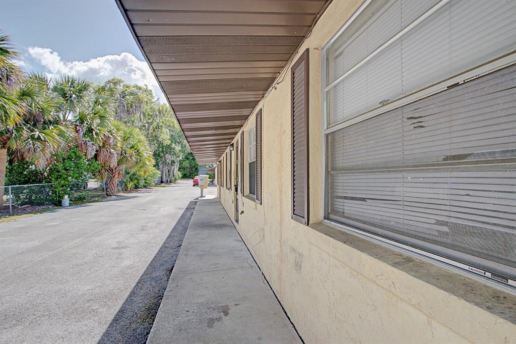 A concrete walkway runs along the side of a beige building with windows and shutters — 830 N CLAKE STREET, DELAND, FL