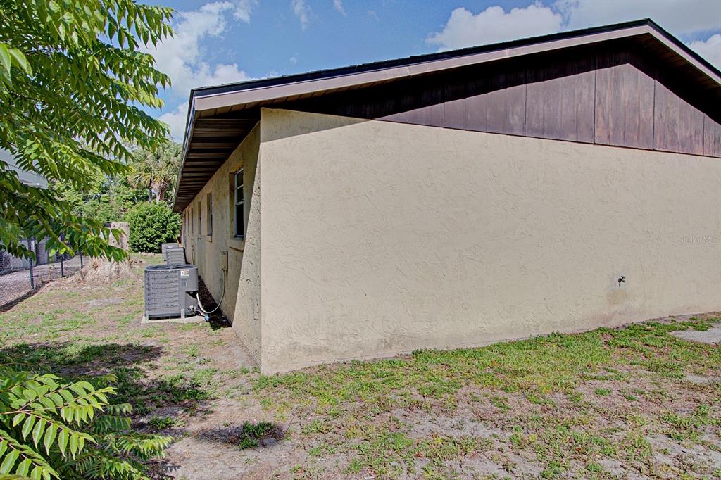 The side exterior of a house features a tan stucco wall, windows, and an air conditioner — 830 N CLAKE STREET, DELAND, FL