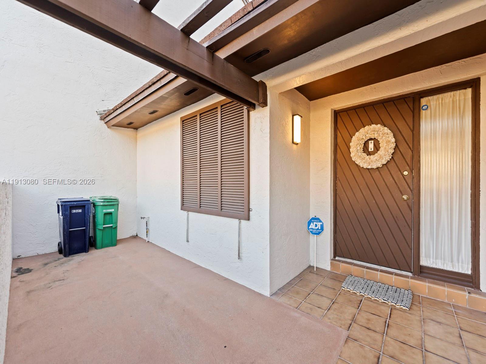 An exterior view of a home entrance with a brown door, shutters, and two trash bins — 13350 SW 91st Ter # C, Miami FL 33186, MIAMI, FL