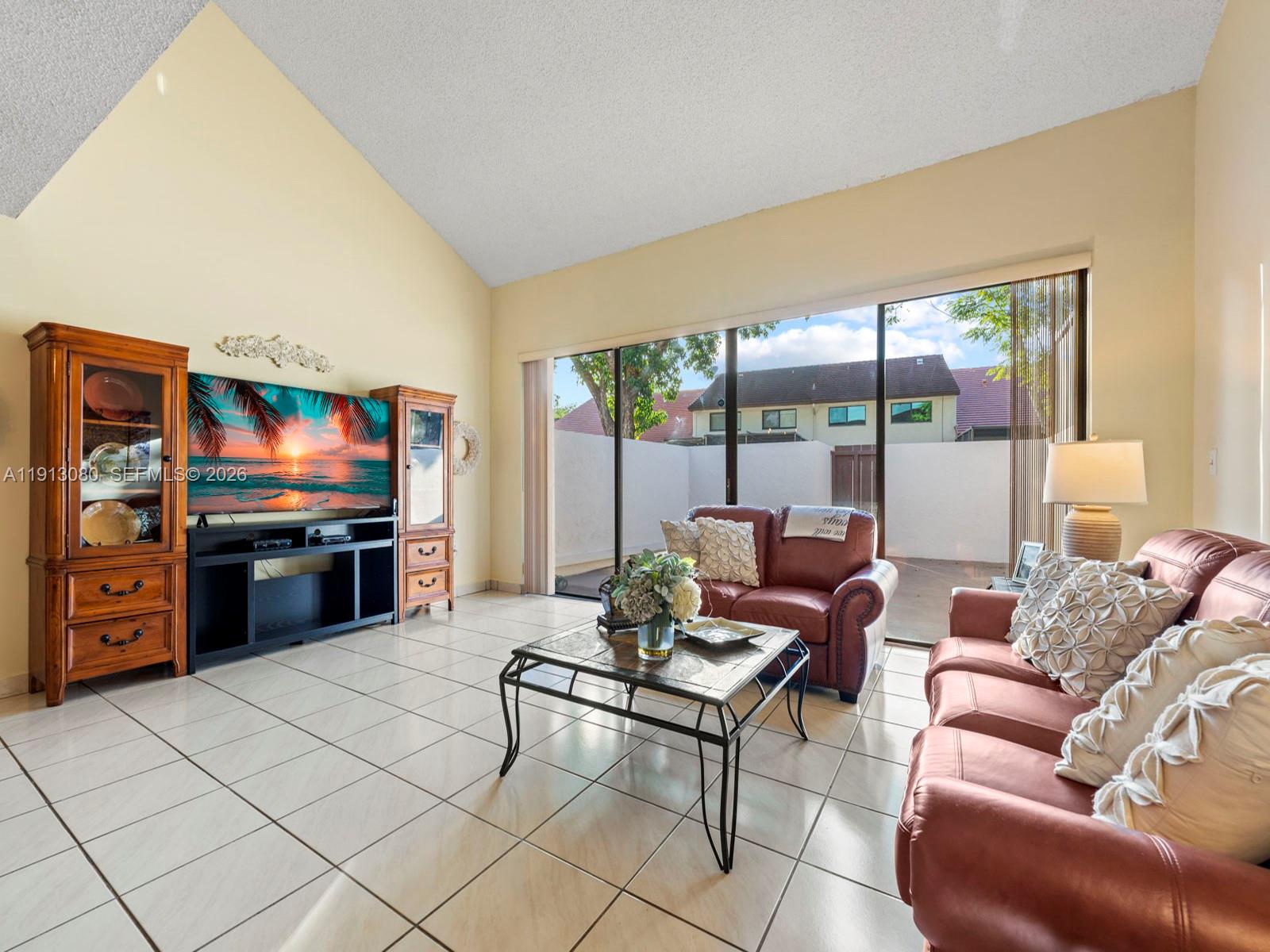 A living room features tile floors, vaulted ceilings, leather furniture, and large sliding glass doors — 13350 SW 91st Ter # C, Miami FL 33186, MIAMI, FL
