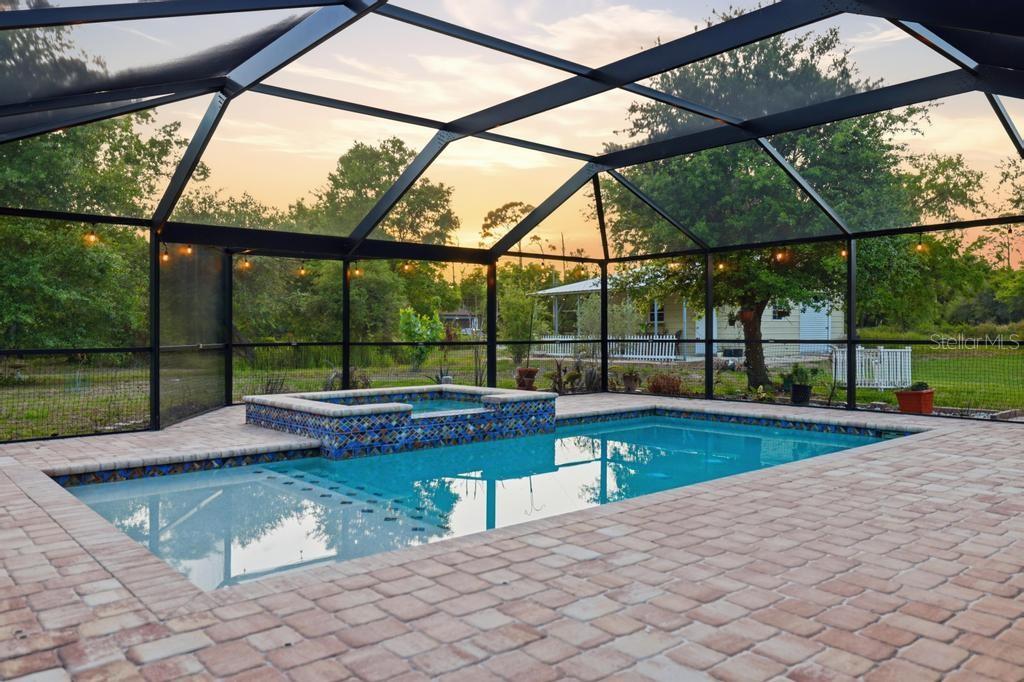 A screened-in swimming pool and hot tub with brick pavers at sunset — 2105 BENNETT LANE, NORTH PORT, FL