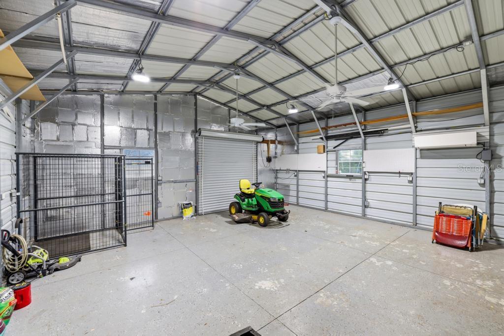 A spacious metal-walled garage features a concrete floor, ceiling fans, and a riding lawn mower — 2105 BENNETT LANE, NORTH PORT, FL