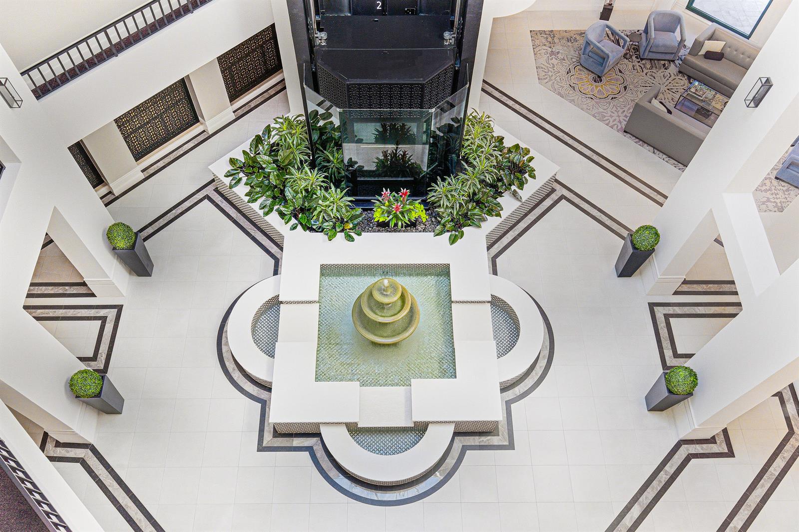 An aerial view of a building atrium featuring a central fountain, plants, and seating areas — 100 SE 5th Avenue, Boca Raton FL 33432, BOCA RATON, FL