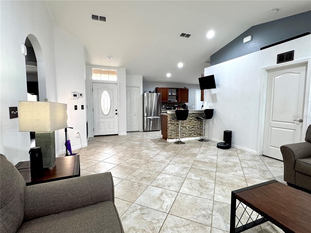 A living room with tile flooring features a kitchen breakfast bar and a front entrance — 248 CHICAGO AVENUE W, HAINES CITY, FL