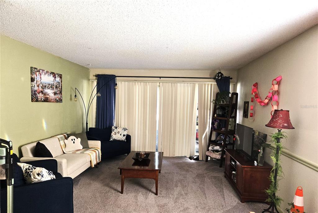 A living room features a beige sofa, dark blue armchairs, a coffee table, and vertical blinds — 6519 W NEWBERRY ROAD UNIT 204, GAINESVILLE, FL