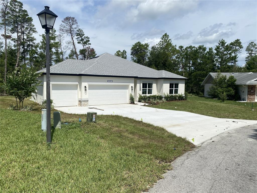 A single-story house with a white exterior, a three-car garage, and a concrete driveway — 8362 NIGHTINGALE ROAD, SPRING HILL, FL