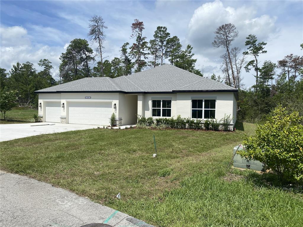 A single-story house with a white stucco exterior, a gray roof, and a three-car garage — 8362 NIGHTINGALE ROAD, SPRING HILL, FL