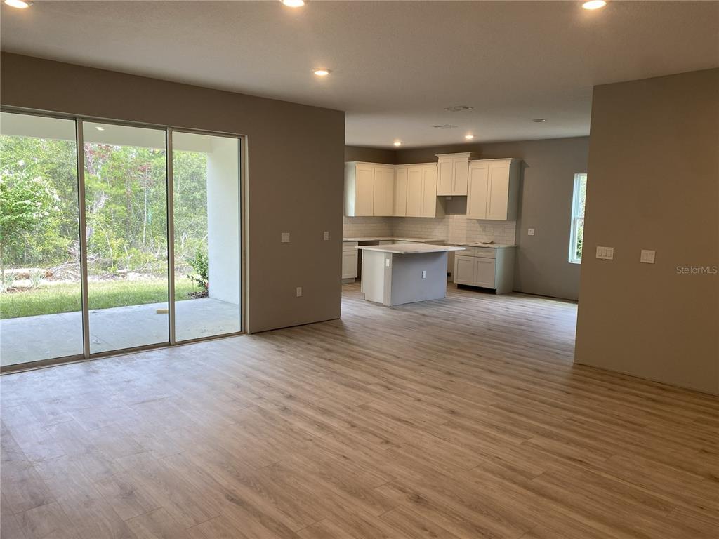 An open-concept living area features light wood-look flooring, a kitchen with white cabinets, and sliding doors — 8362 NIGHTINGALE ROAD, SPRING HILL, FL